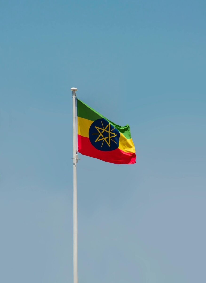 Ethiopian national flag elegantly swaying on a flagpole against a clear blue sky in Addis Ababa.