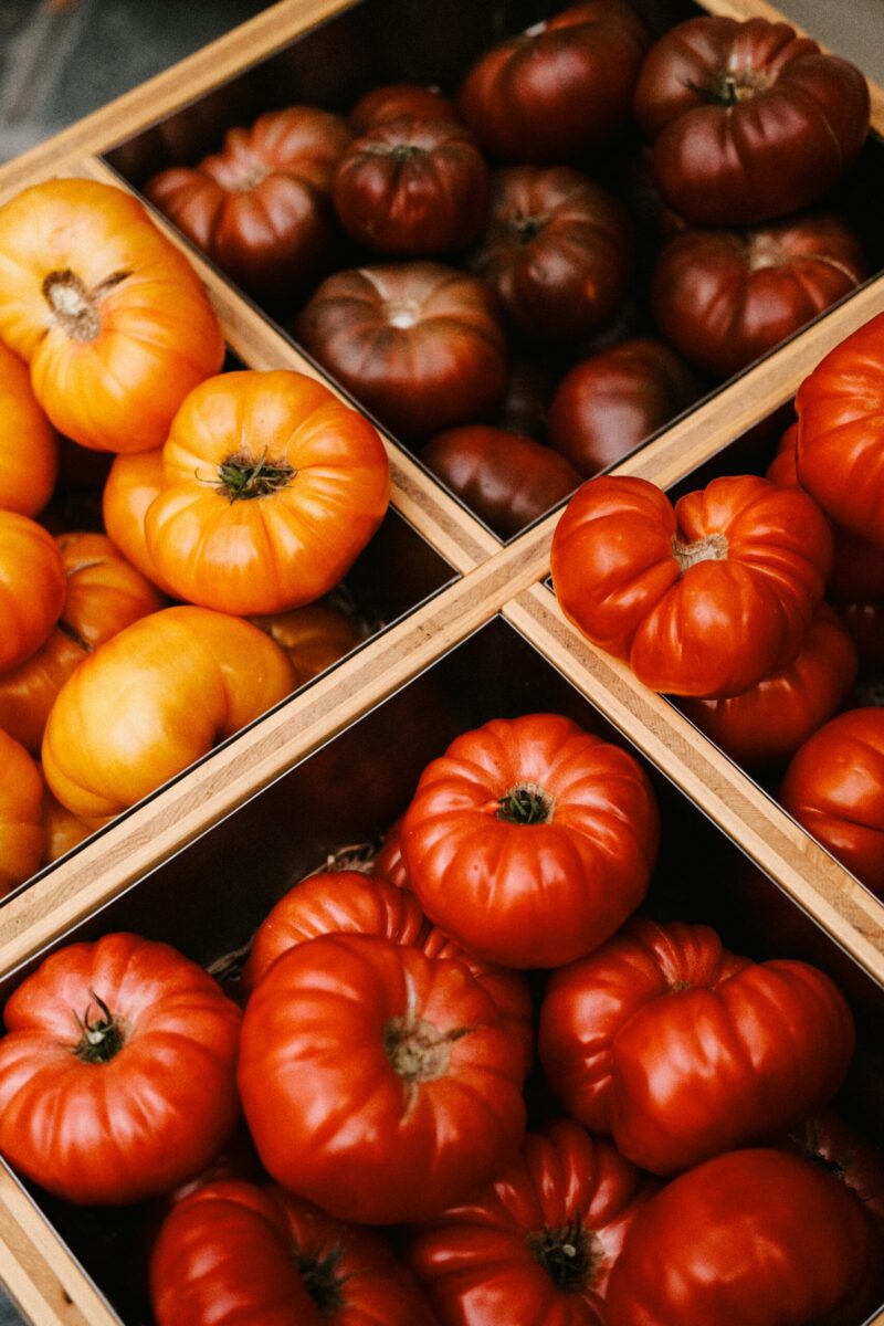 A vibrant assortment of red, yellow, and brown heirloom tomatoes in wooden crates, ideal for food photography