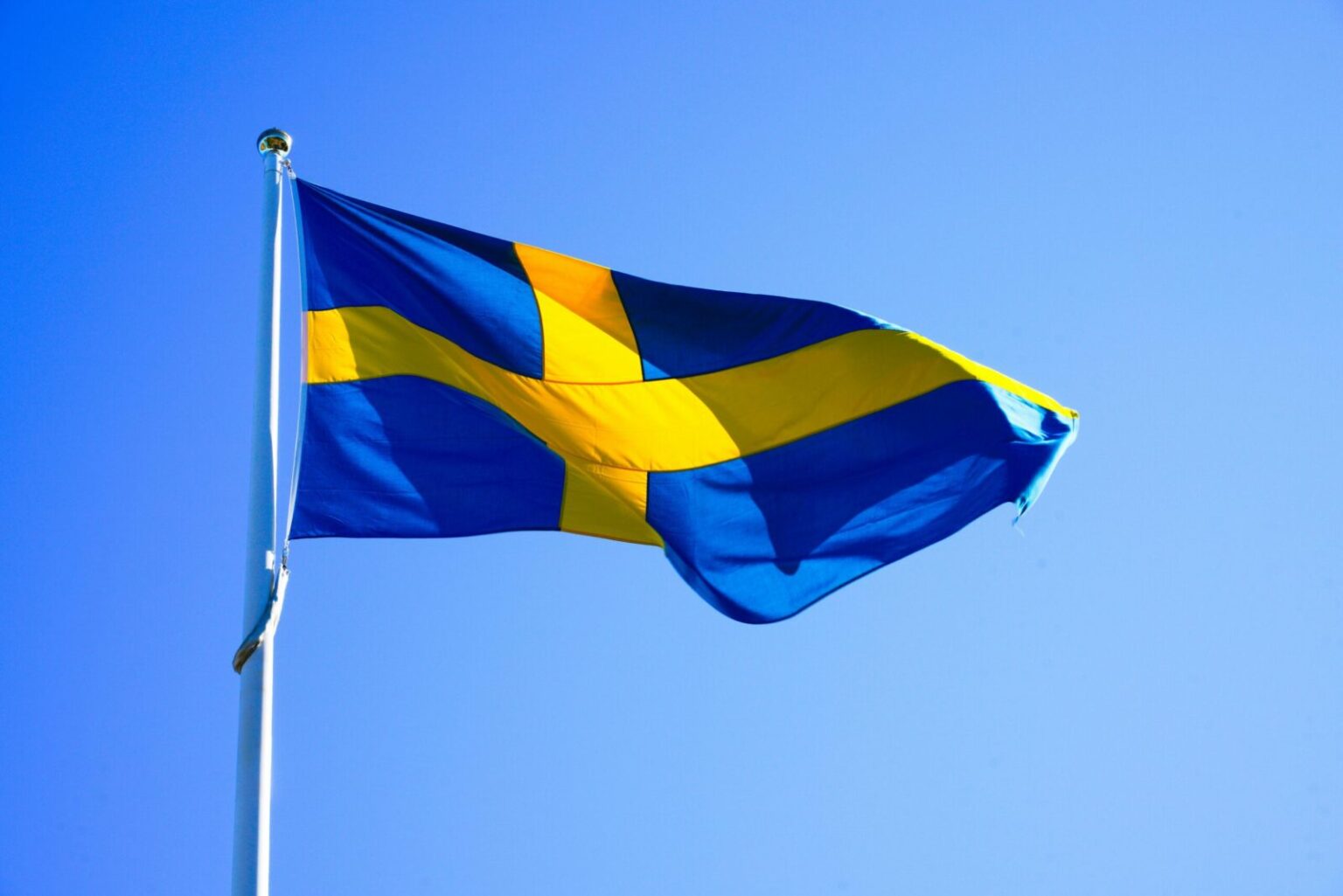 Bright Swedish flag waving on a clear day with blue sky.