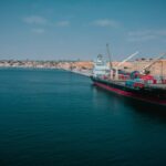 Cargo ship docked at Namibe port in Angola with shipping containers and cranes.