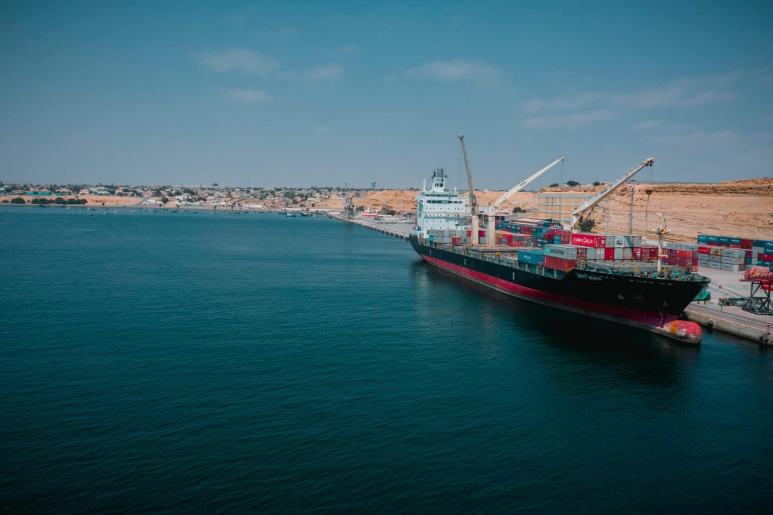 Cargo ship docked at Namibe port in Angola with shipping containers and cranes.