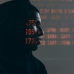 Side profile of a man in a hoodie, surrounded by red code, depicting cybersecurity theme.