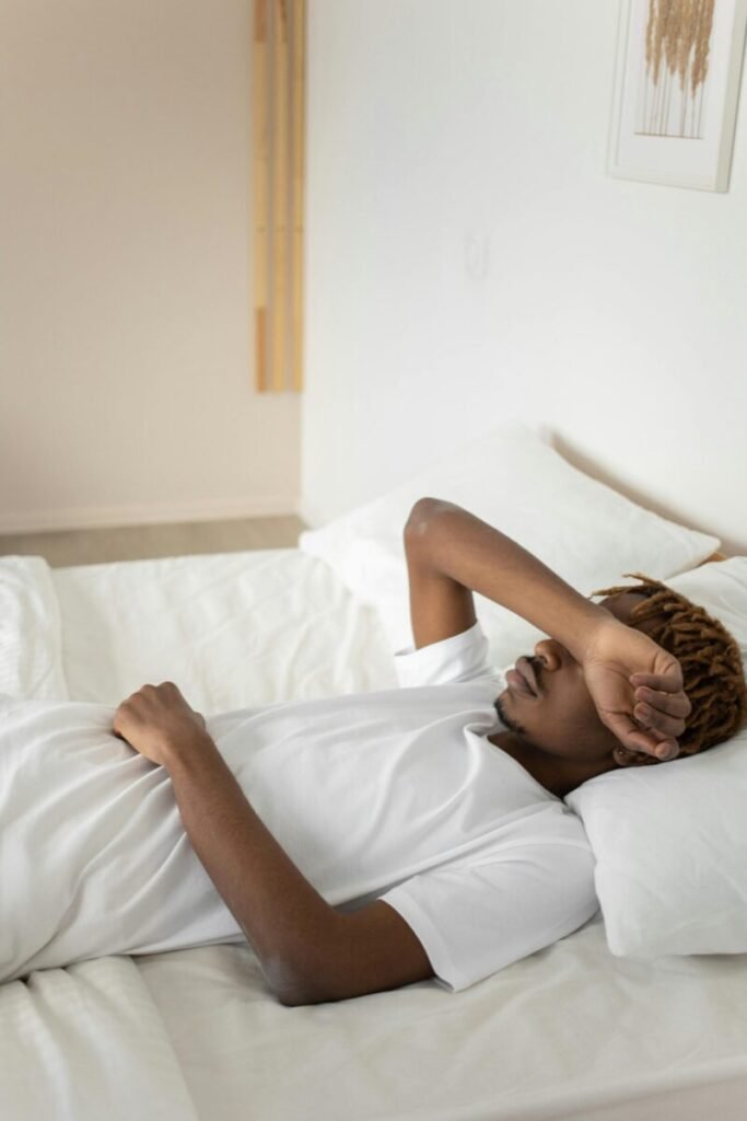 Young man relaxing in a minimalist white bedroom, symbolizing tranquility and rest.