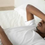 Young man relaxing in a minimalist white bedroom, symbolizing tranquility and rest.