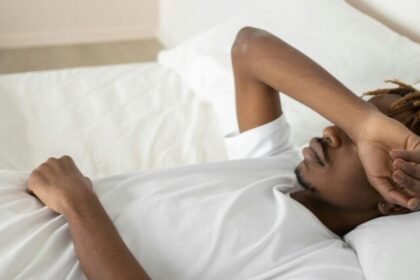 Young man relaxing in a minimalist white bedroom, symbolizing tranquility and rest.