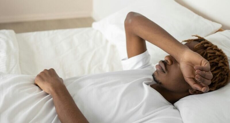 Young man relaxing in a minimalist white bedroom, symbolizing tranquility and rest.
