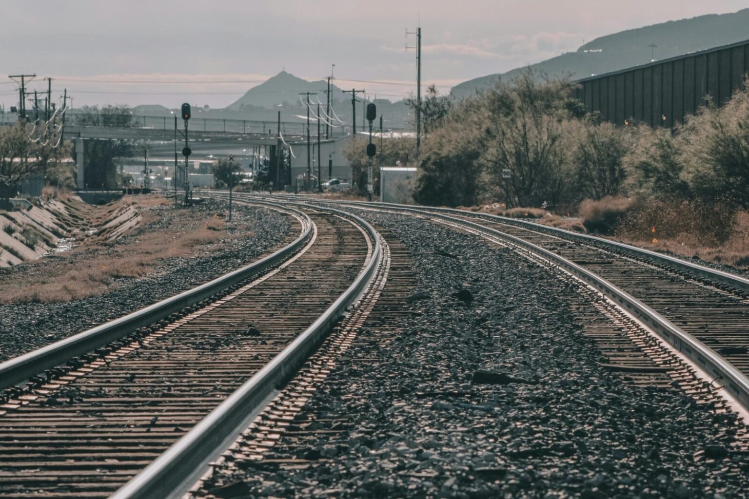 Curving railway tracks stretch across a scenic landscape under a clear sky. Captured outdoors.