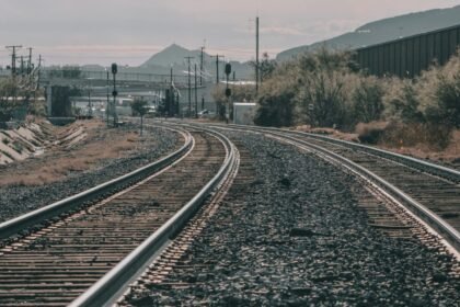 Curving railway tracks stretch across a scenic landscape under a clear sky. Captured outdoors.