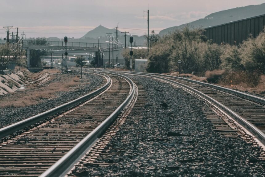 Curving railway tracks stretch across a scenic landscape under a clear sky. Captured outdoors.