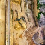 An aerial shot of an open-pit mine with machinery and pathways visible, surrounded by landscape.