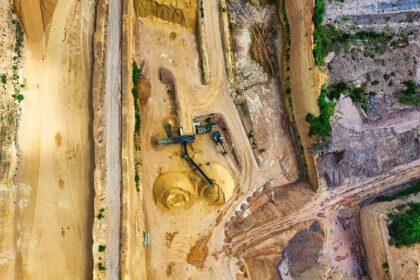 An aerial shot of an open-pit mine with machinery and pathways visible, surrounded by landscape.