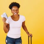 Cheerful woman holding passport ready for travel against a vibrant yellow backdrop.