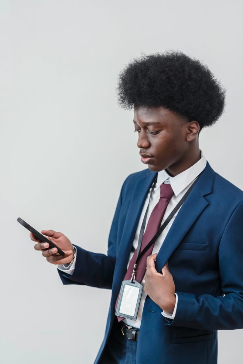 A young black man in a suit using a smartphone against a white background. Studio shot.