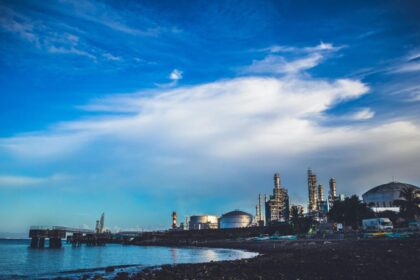 Industrial buildings by the sea under a dramatic cloudy sky.