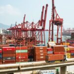 A bustling scene of cargo containers and cranes at a Hong Kong port, showcasing global trade.