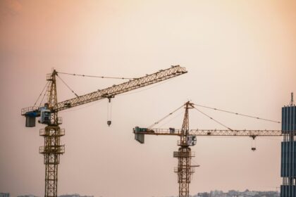 Skyline view of an urban construction site with prominent tower cranes at dusk.