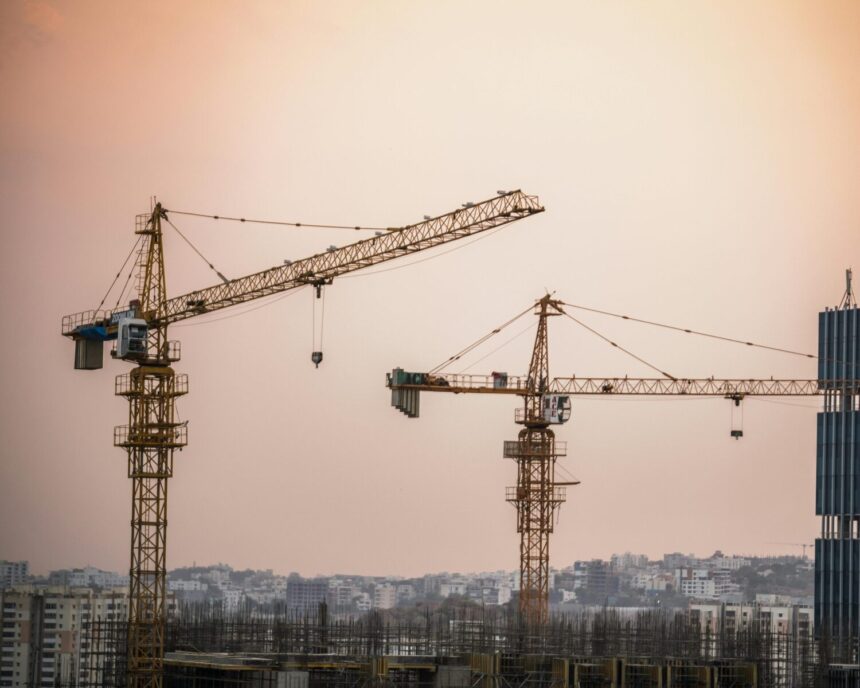 Skyline view of an urban construction site with prominent tower cranes at dusk.