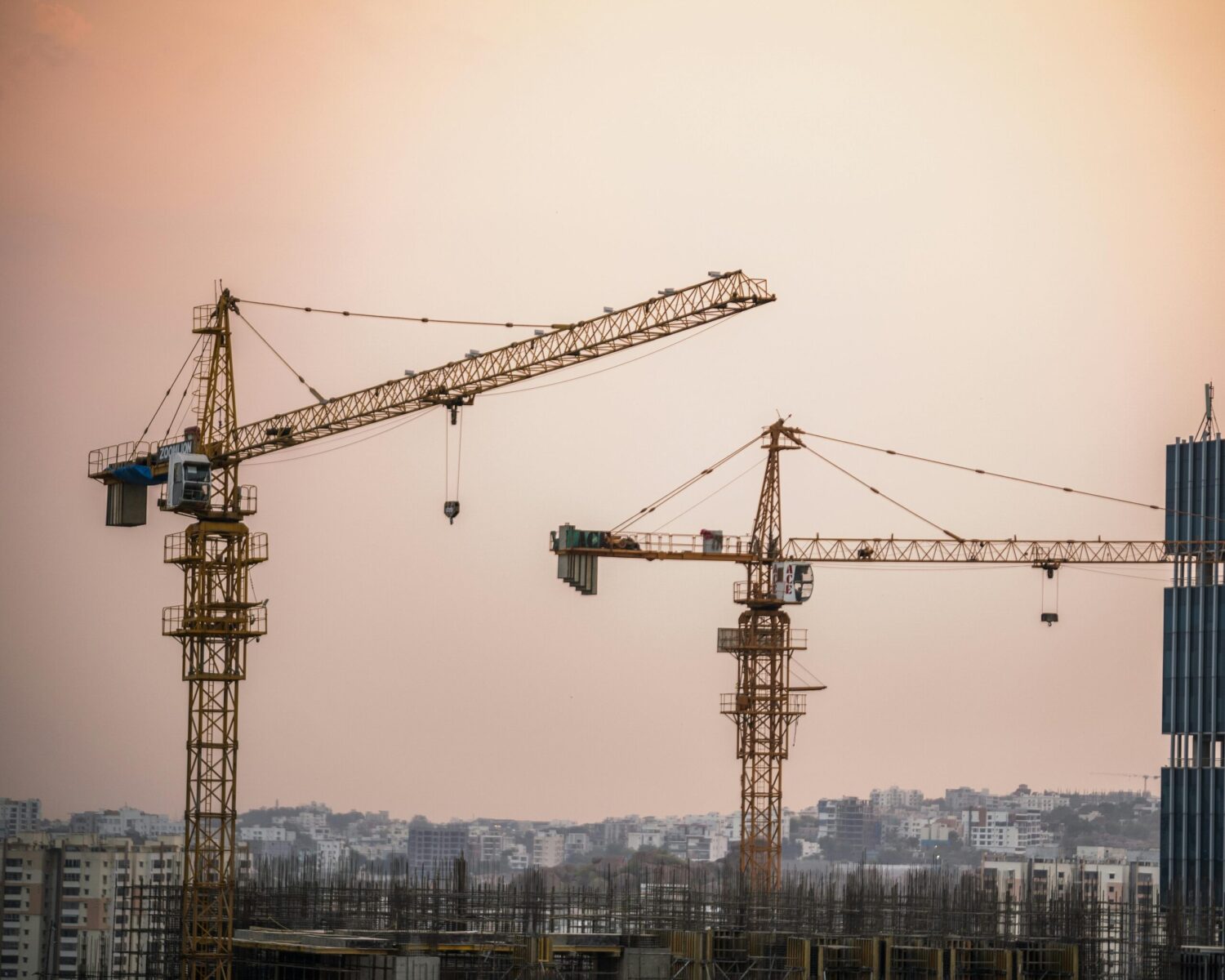 Skyline view of an urban construction site with prominent tower cranes at dusk.