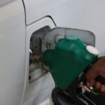 Close-up of a hand refilling a car's gas tank at a station with a green fuel nozzle.