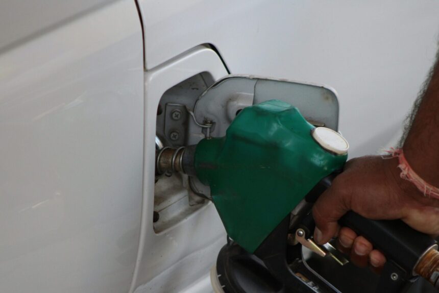Close-up of a hand refilling a car's gas tank at a station with a green fuel nozzle.
