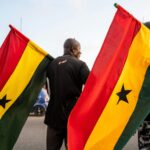 Two men holding Ghanaian flags during a public event in Ghana, capturing national pride.