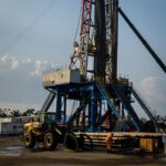 Oil rig in action during sunset, featuring heavy machinery and a lone worker on site.