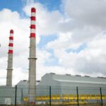 Factory chimneys against a blue sky symbolize industrial power and environmental impact.