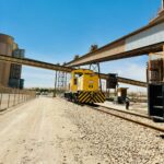 A yellow industrial train at a cement factory track in Saudi Arabia under a clear blue sky.