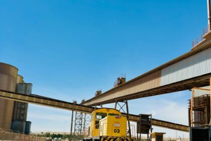 A yellow industrial train at a cement factory track in Saudi Arabia under a clear blue sky.