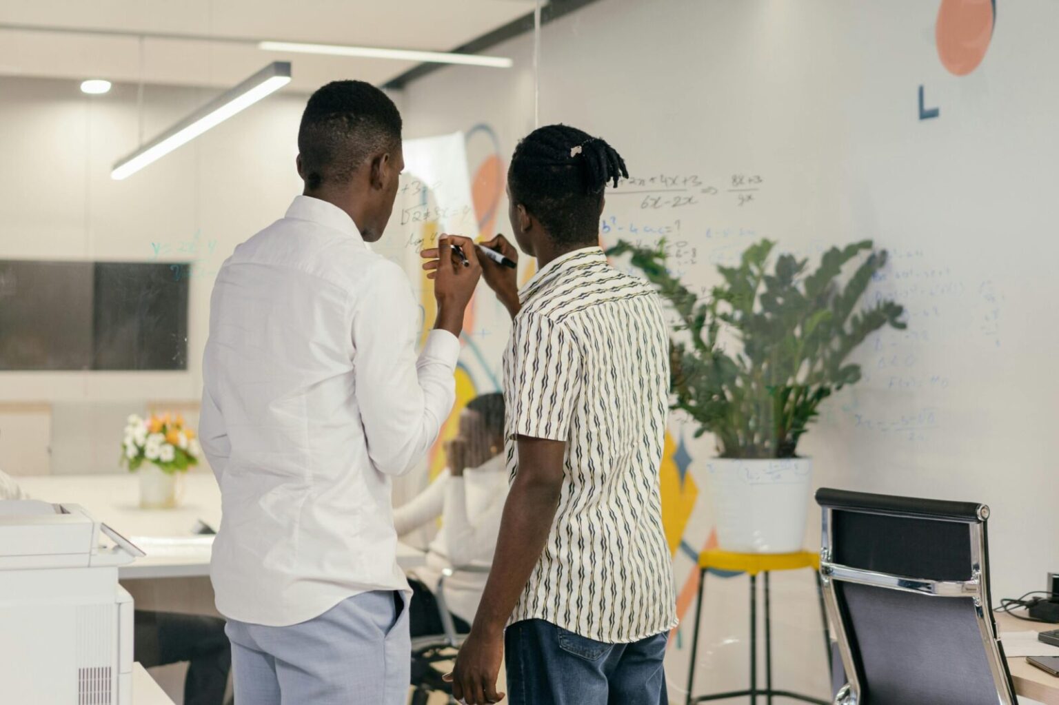Colleagues brainstorming and writing on a glass board in modern office.