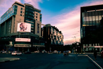 A bustling city street with modern skyscrapers and vehicles at sunset, Gautrain Hotel visible.
