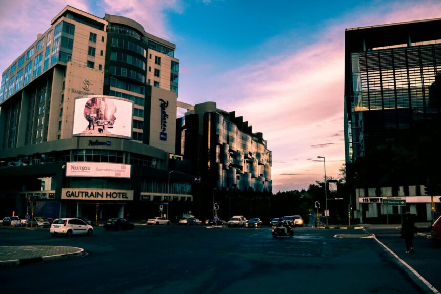 A bustling city street with modern skyscrapers and vehicles at sunset, Gautrain Hotel visible.