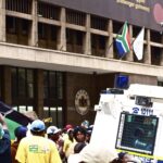 A protest with a police officer photographing the crowd in urban South Africa.
