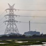Electric tower in a marshland with a factory in the distance, creating a mix of nature and industry.