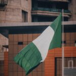 Nigerian flag fluttering against a modern city building backdrop, symbolizing national pride.