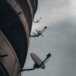Satellite dishes against a cloudy sky create a moody urban scene.