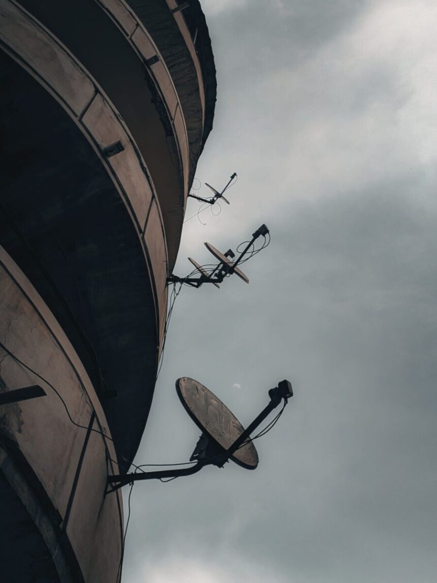 Satellite dishes against a cloudy sky create a moody urban scene.